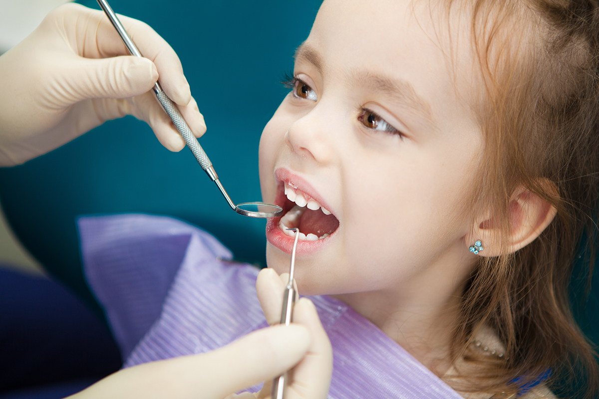 a doctor helping a child during a check up while explaining when should a child go to the dentist